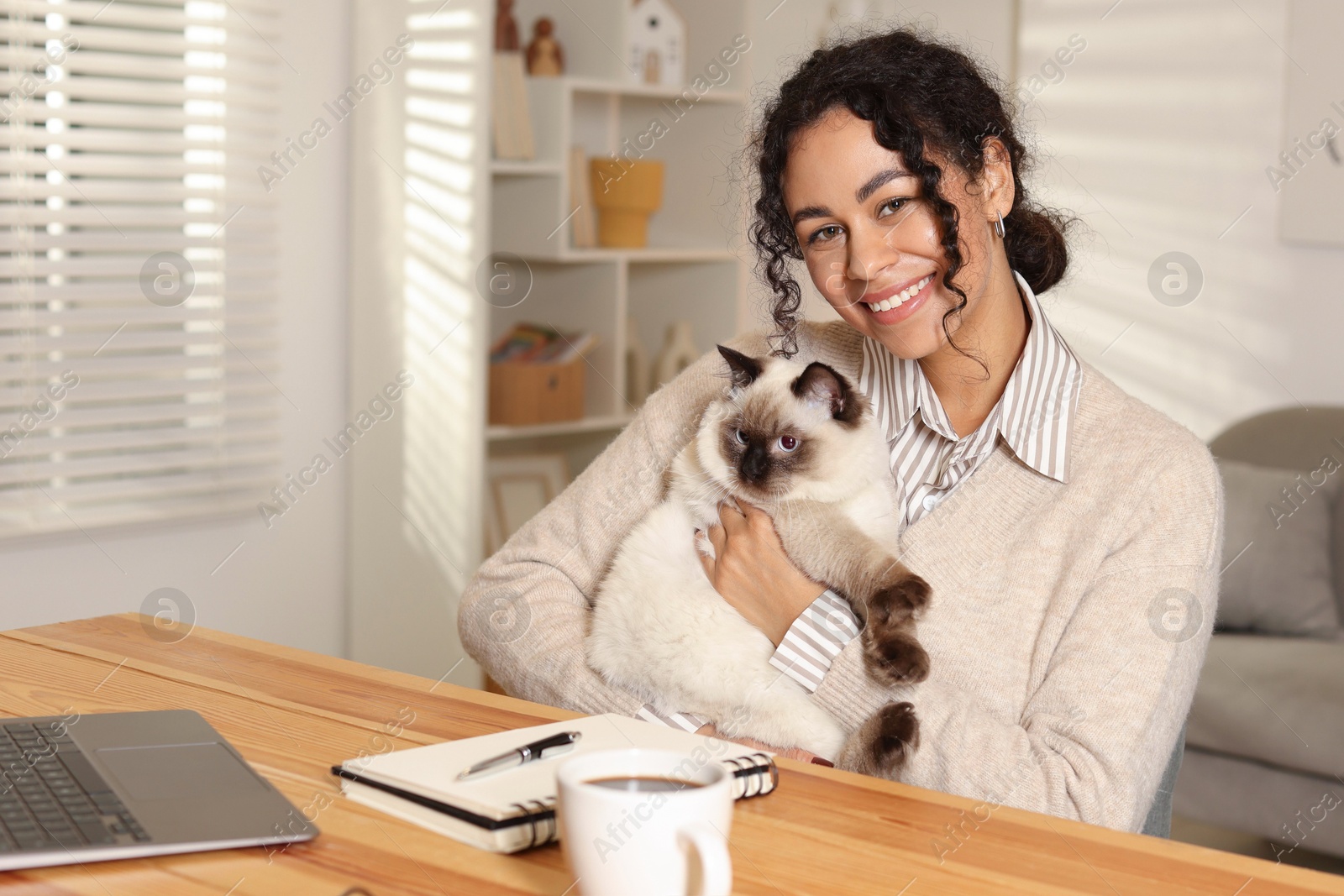 Photo of Beautiful woman with her cute cat working on laptop at desk in home office