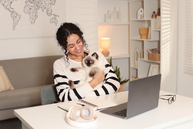 Beautiful woman with her cute cat working on laptop at desk in home office