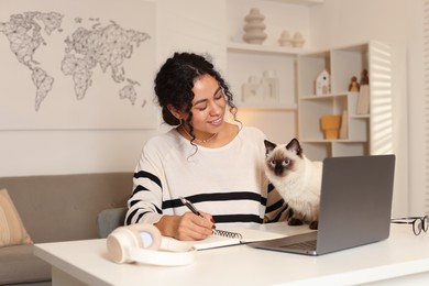 Photo of Beautiful woman with her cute cat working on laptop at desk in home office