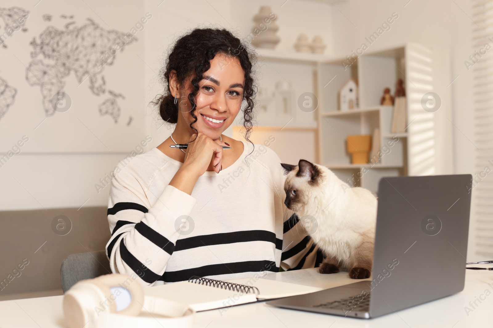 Photo of Beautiful woman with her cute cat working on laptop at desk in home office