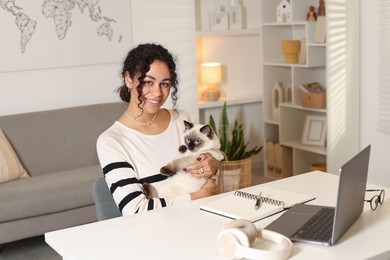 Photo of Beautiful woman with her cute cat working on laptop at desk in home office