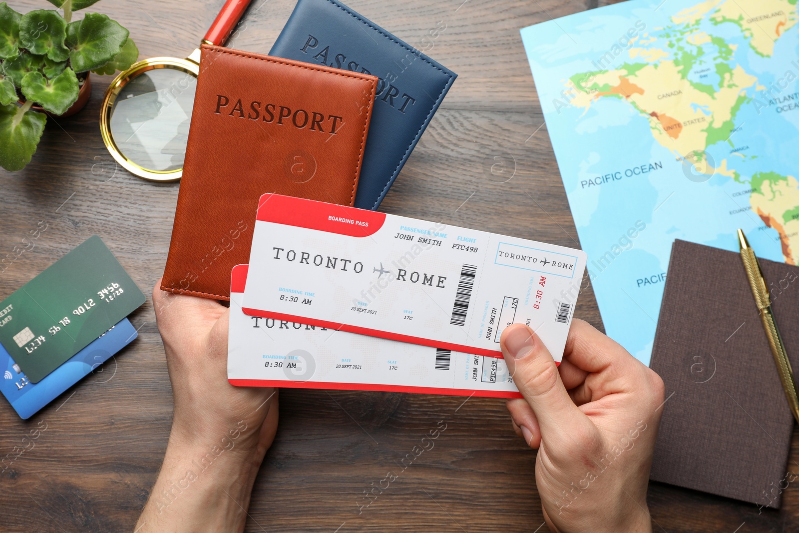 Photo of Travel agency. Man holding passports and flight tickets at wooden table, top view