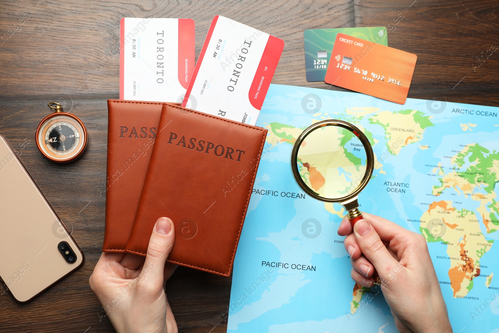 Photo of Travel agency. Woman with flight tickets and passports looking at world map through magnifying glass at wooden table, top view