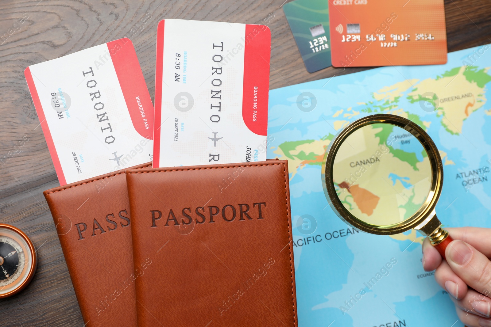 Photo of Travel agency. Woman with flight tickets and passports looking at world map through magnifying glass at wooden table, top view