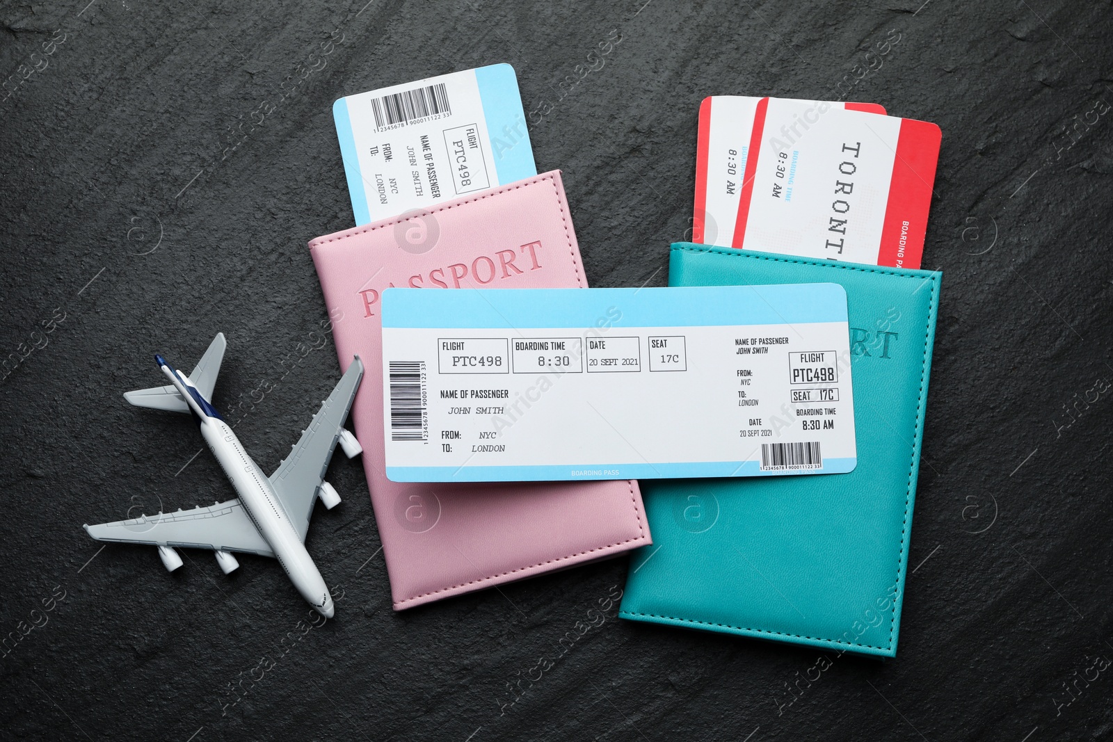 Photo of Travel agency. Flight tickets, passports and plane model on dark textured table, flat lay