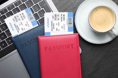 Photo of Travel agency. Flight tickets, passports, laptop and cup of coffee on dark textured table, flat lay