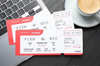 Photo of Travel agency. Flight tickets, laptop and cup of coffee on dark textured table, flat lay