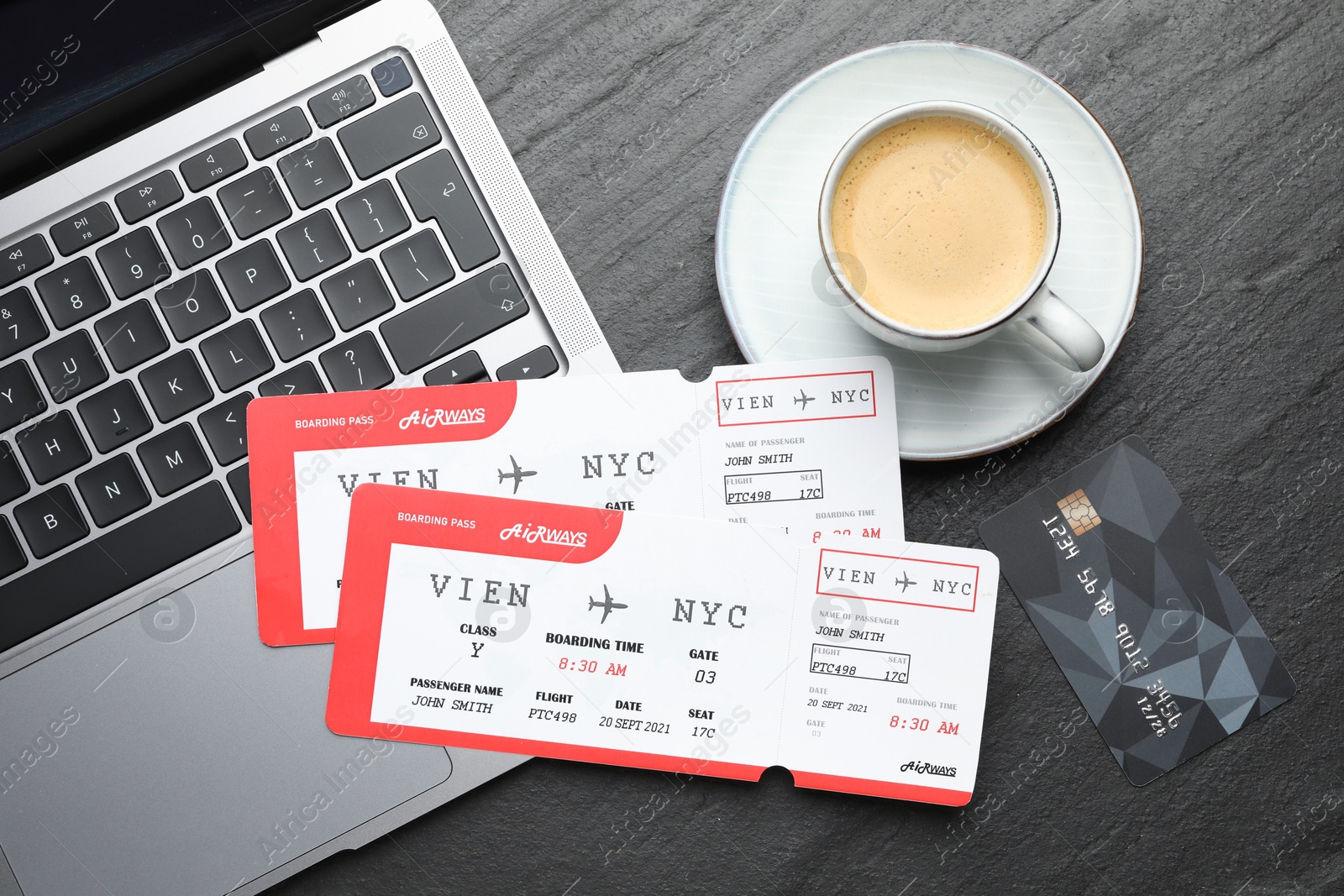 Photo of Travel agency. Flight tickets, laptop, credit card and cup of coffee on dark textured table, flat lay