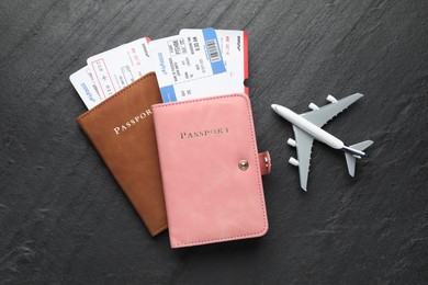 Photo of Travel agency. Flight tickets, passports and plane model on dark textured table, flat lay