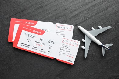 Photo of Travel agency. Flight tickets and plane model on dark textured table, flat lay