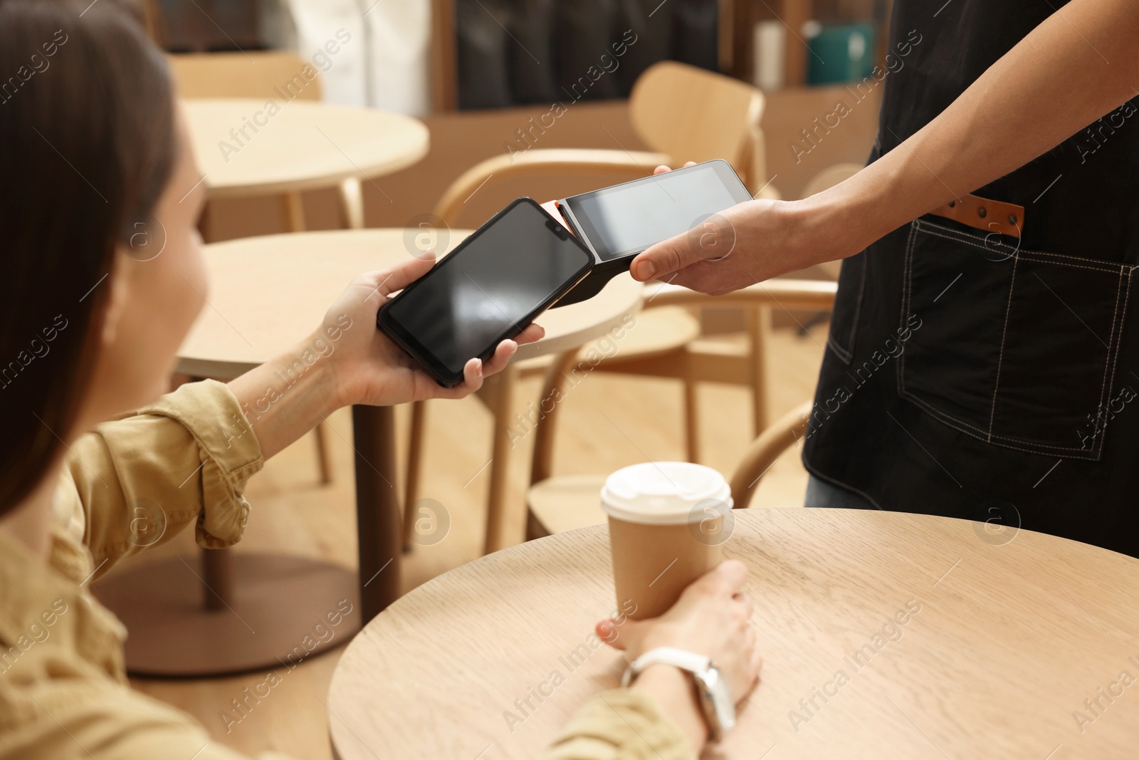 Photo of Woman paying with smartphone via terminal at wooden table in cafe, closeup