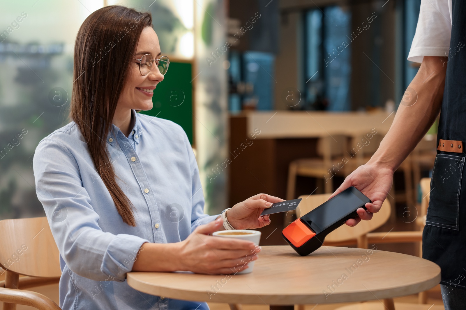 Photo of Woman paying with credit card via terminal at wooden table in cafe