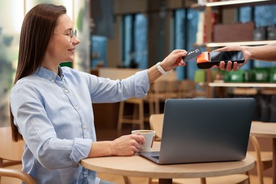 Photo of Woman paying with credit card via terminal at wooden table in cafe