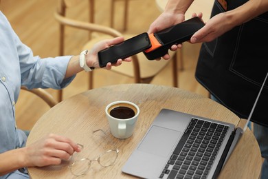 Photo of Woman paying with smartphone via terminal at wooden table in cafe, closeup