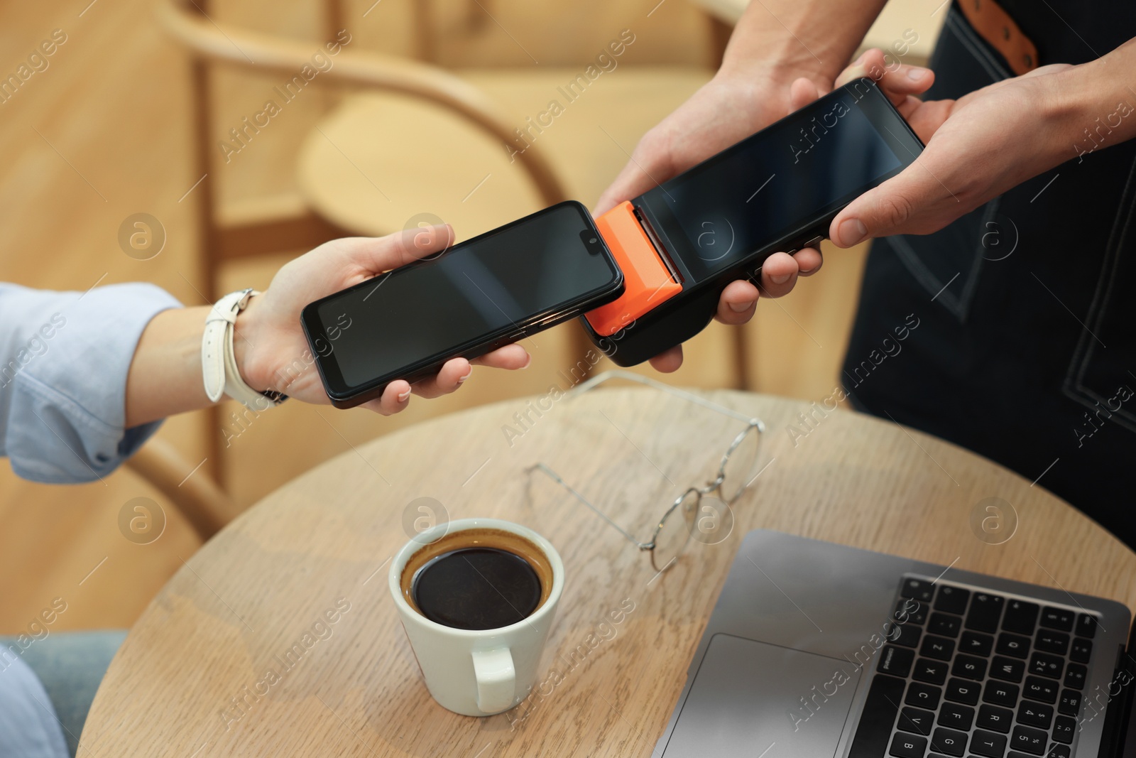 Photo of Woman paying with smartphone via terminal at wooden table in cafe, closeup