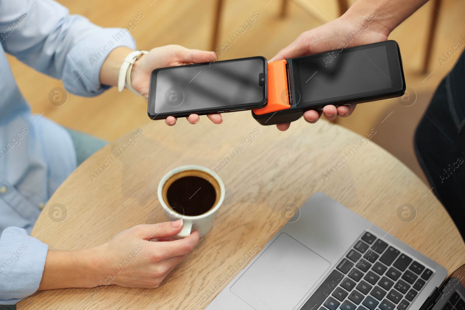 Photo of Woman paying with smartphone via terminal at wooden table in cafe, closeup