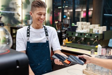 Photo of Cafe worker taking payment from client via terminal indoors