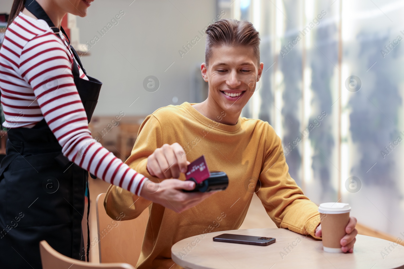 Photo of Man paying with credit card via terminal at wooden table in cafe