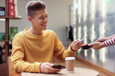 Photo of Man paying with credit card via terminal at wooden table in cafe