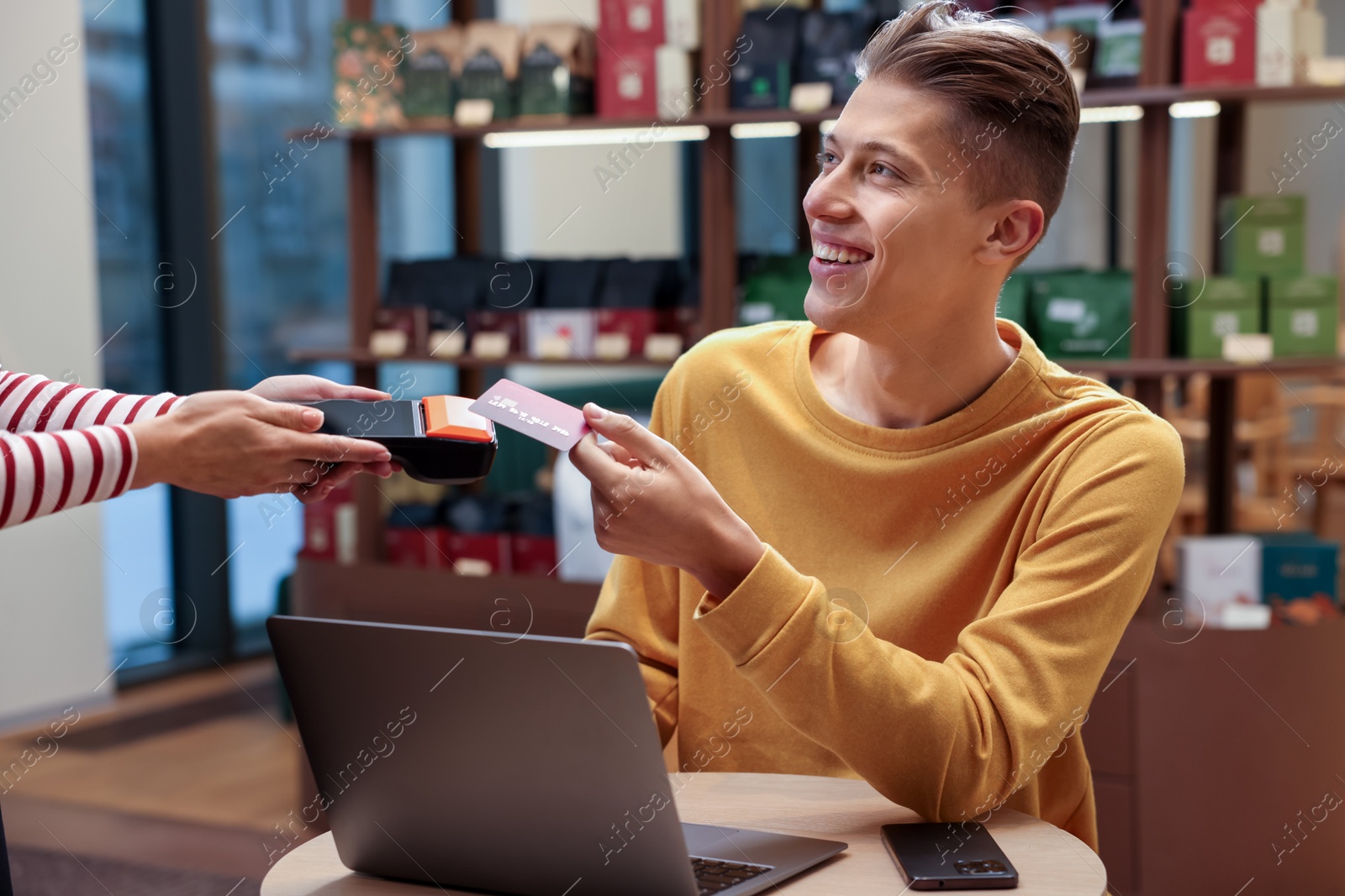 Photo of Man paying with credit card via terminal at wooden table in cafe