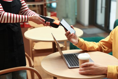 Photo of Man paying with smartphone via terminal at wooden table in cafe, closeup