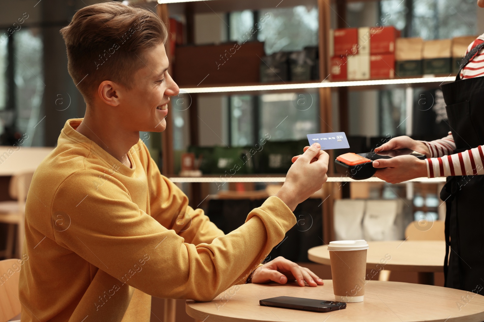 Photo of Man paying with credit card via terminal at wooden table in cafe