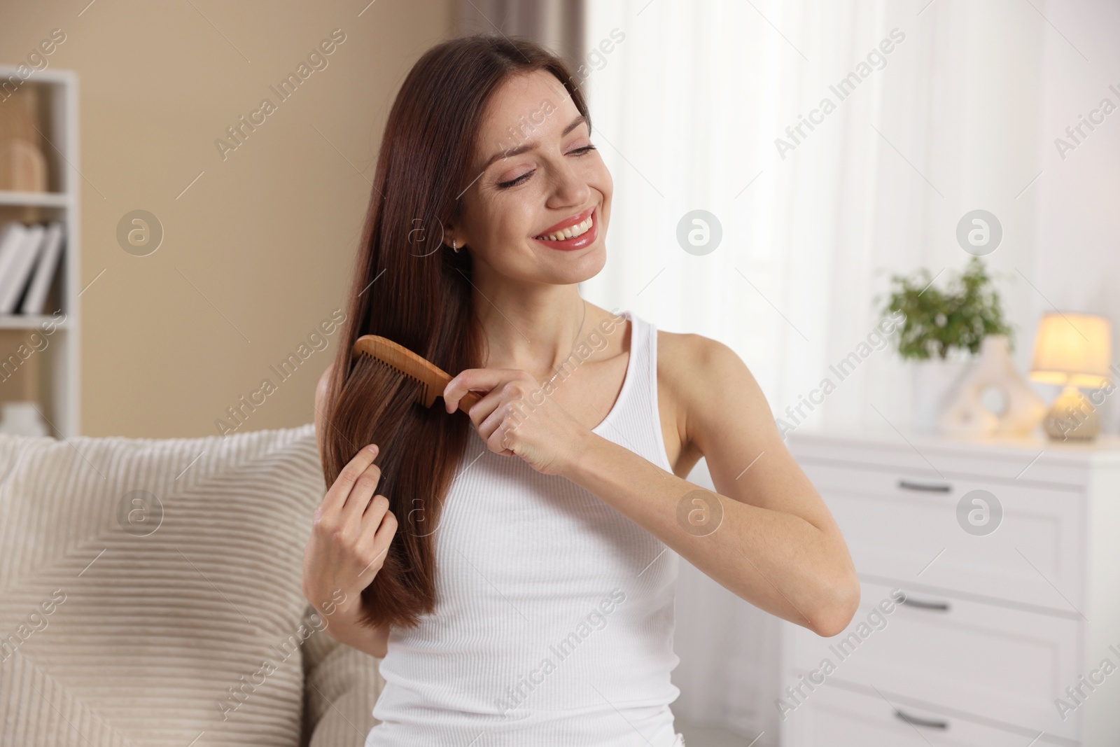 Photo of Smiling woman brushing her hair with comb at home