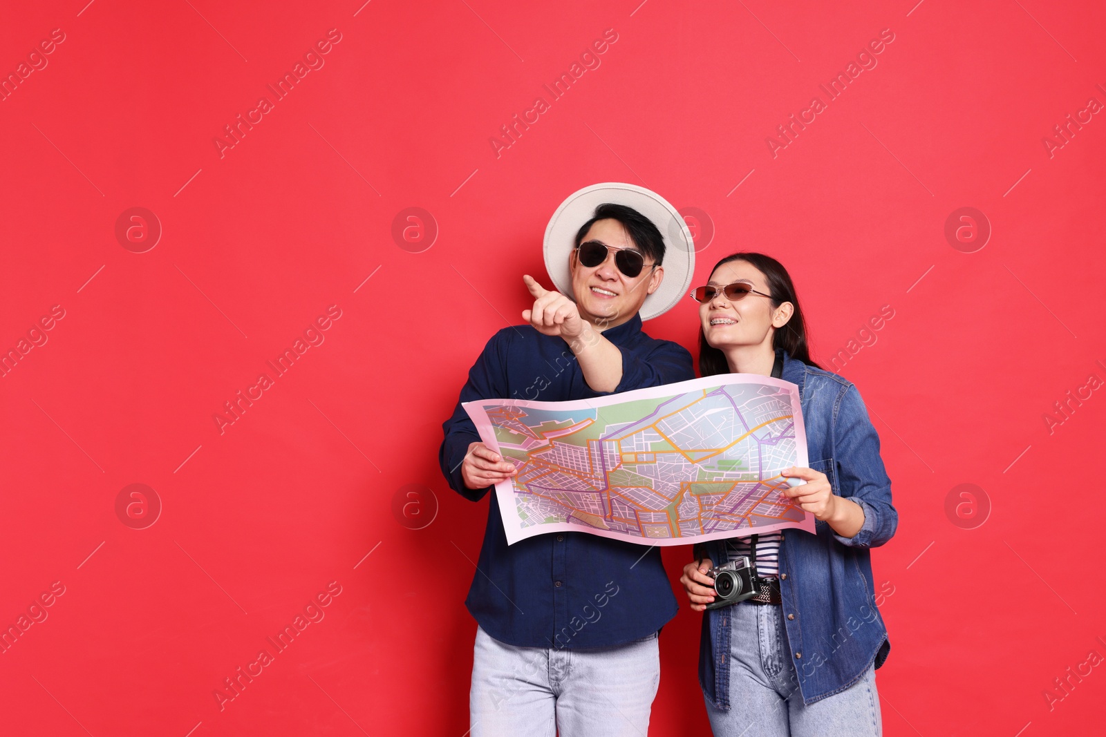 Photo of Happy travellers with map on red background. Space for text