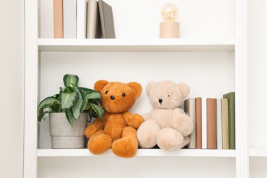 Photo of Cute teddy bears, books and houseplant on shelf indoors