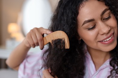 Smiling young woman brushing her curly hair with comb indoors