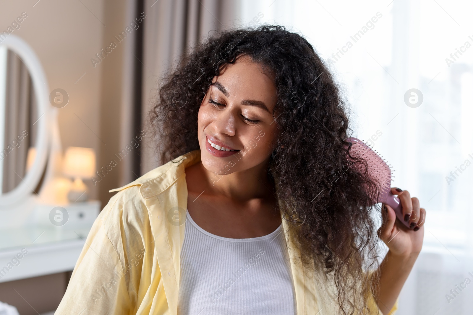 Photo of Smiling young woman brushing her curly hair at home