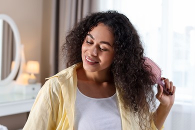 Photo of Smiling young woman brushing her curly hair at home