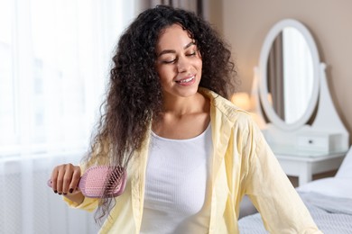 Photo of Smiling young woman brushing her curly hair at home