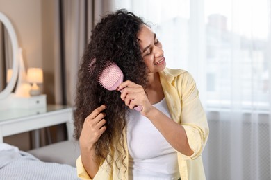 Photo of Smiling young woman brushing her curly hair at home