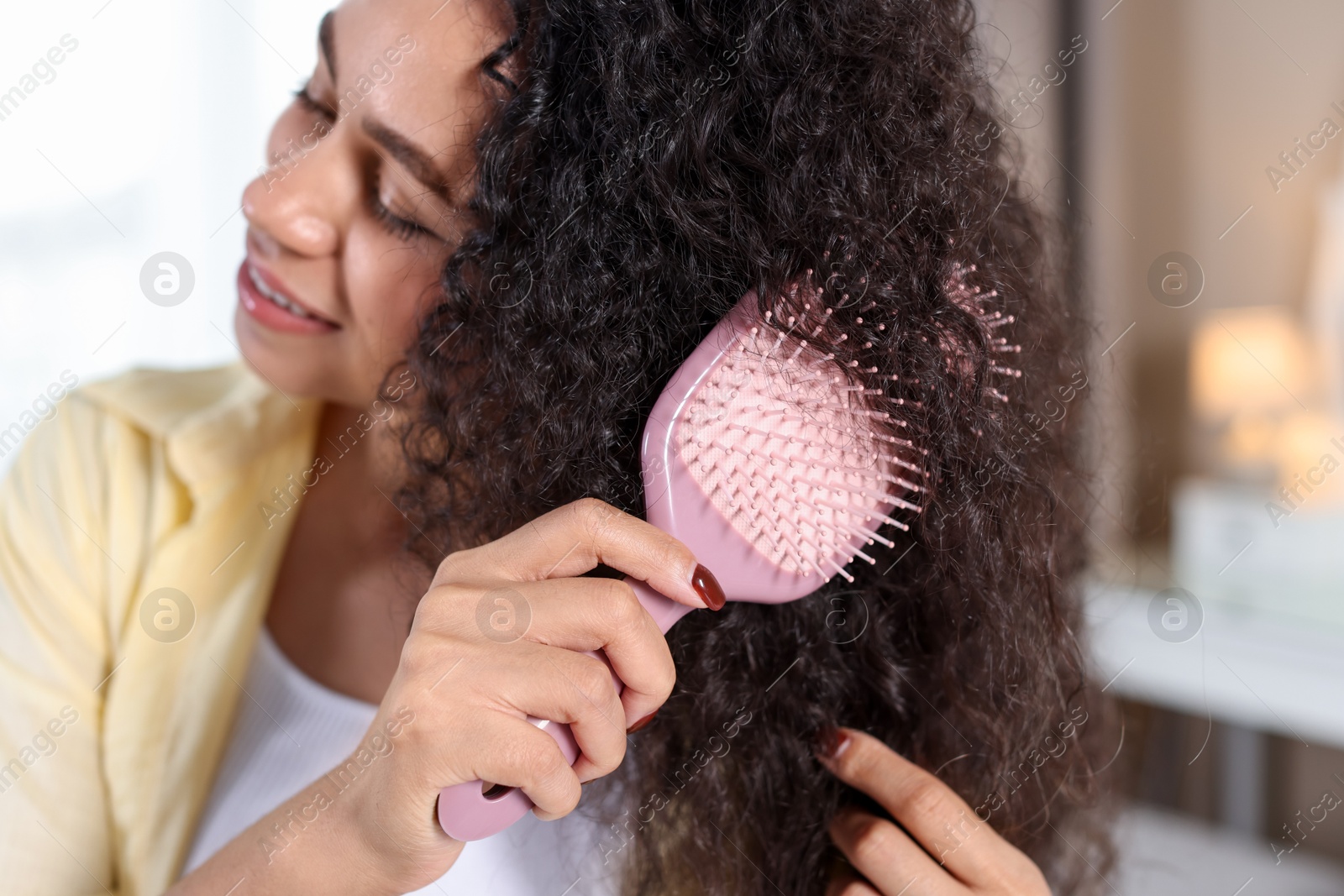 Photo of Young woman brushing her curly hair indoors. Selective focus