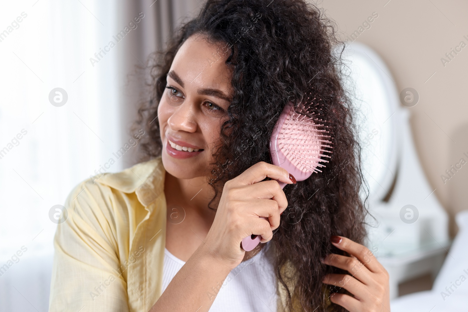 Photo of Smiling young woman brushing her curly hair at home