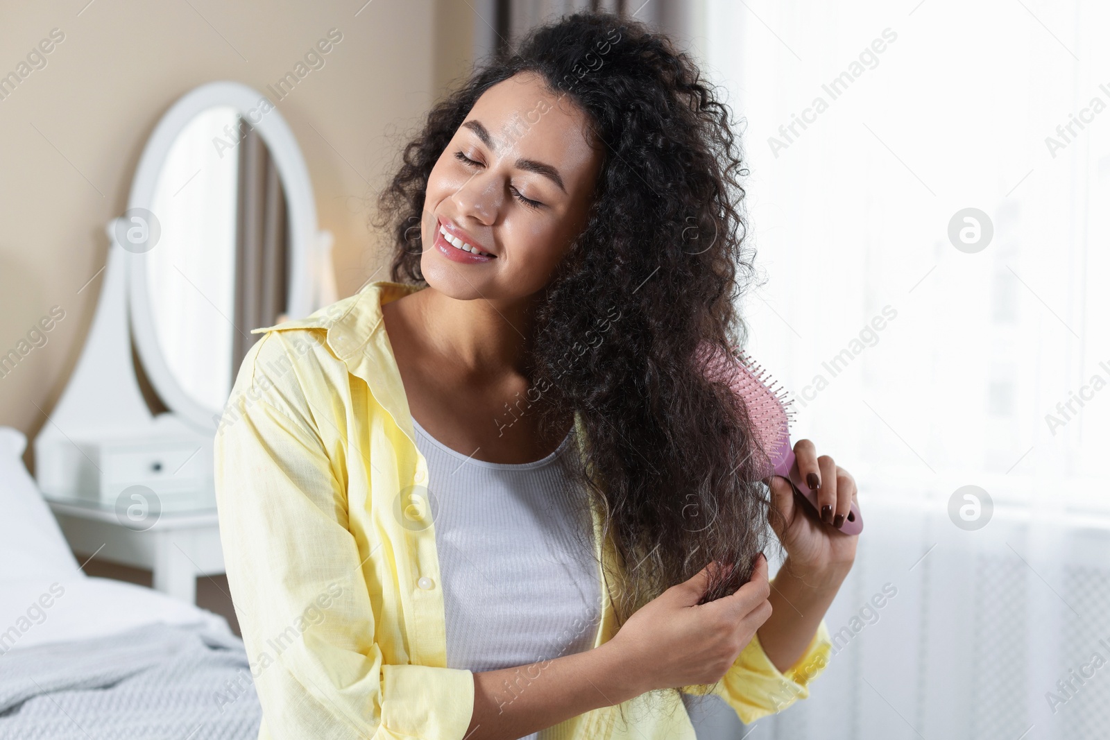 Photo of Smiling young woman brushing her curly hair at home