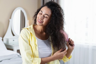 Photo of Smiling young woman brushing her curly hair at home