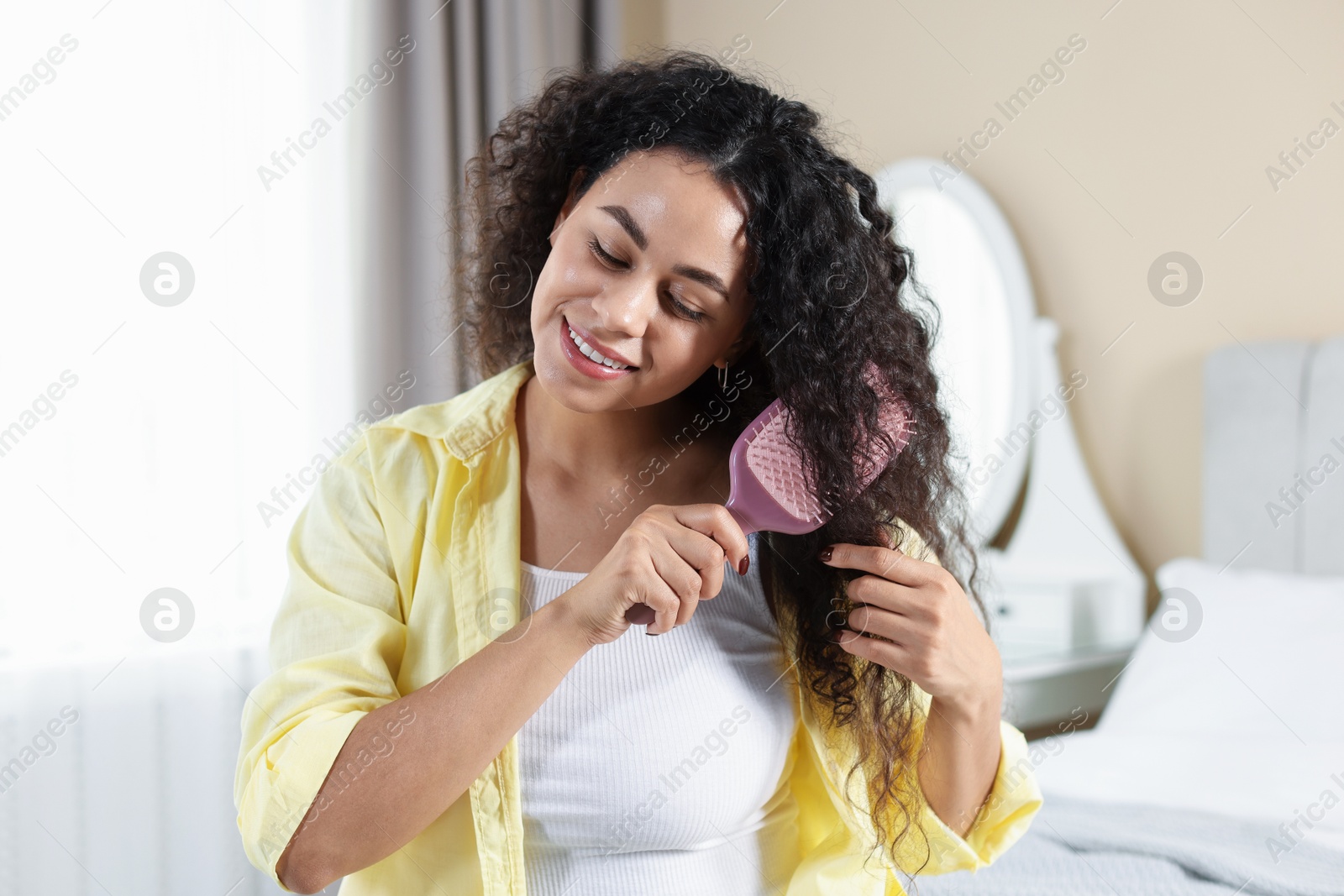 Photo of Smiling young woman brushing her curly hair at home