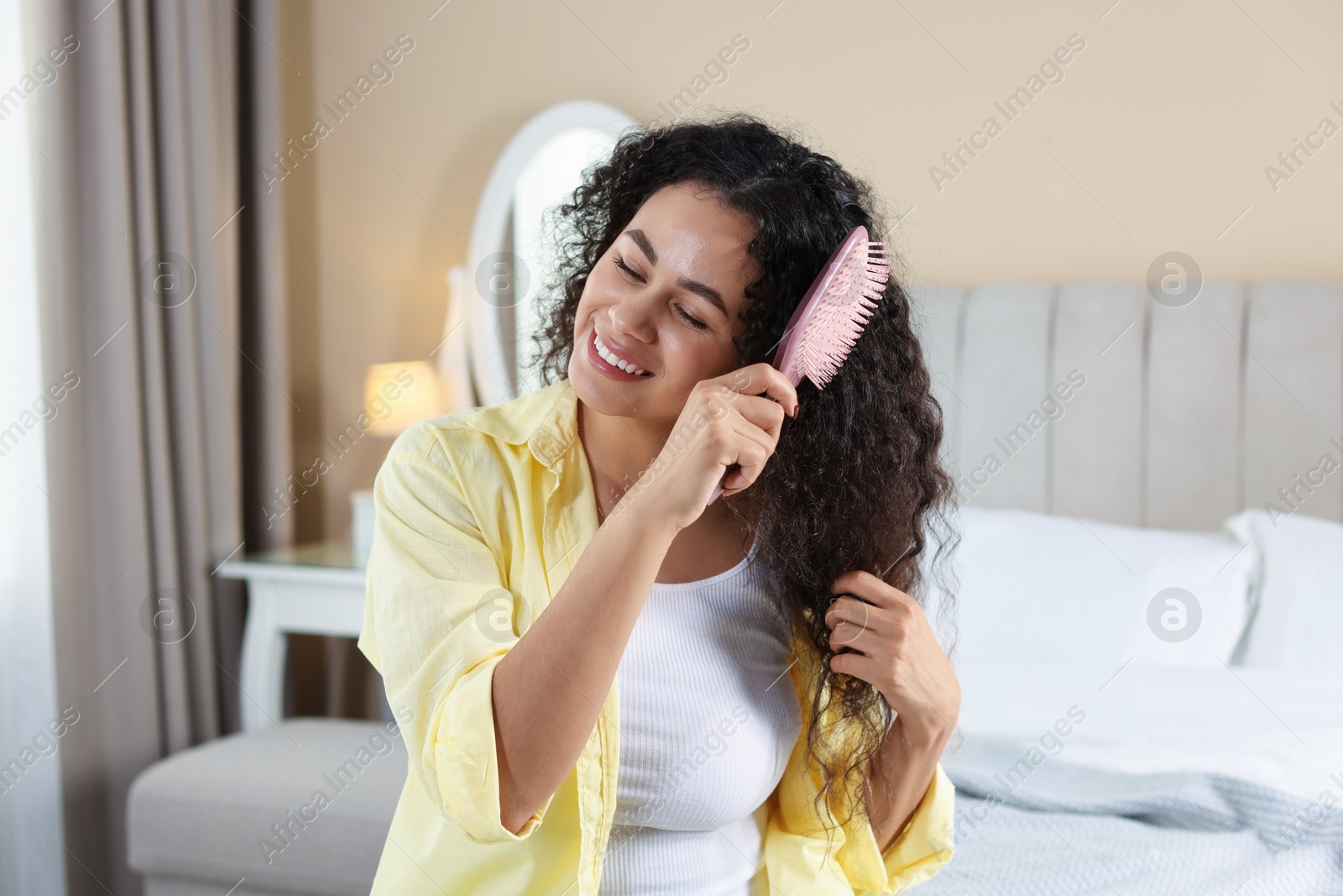 Photo of Smiling young woman brushing her curly hair at home