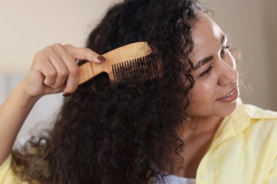 Photo of Young woman brushing her curly hair with comb indoors