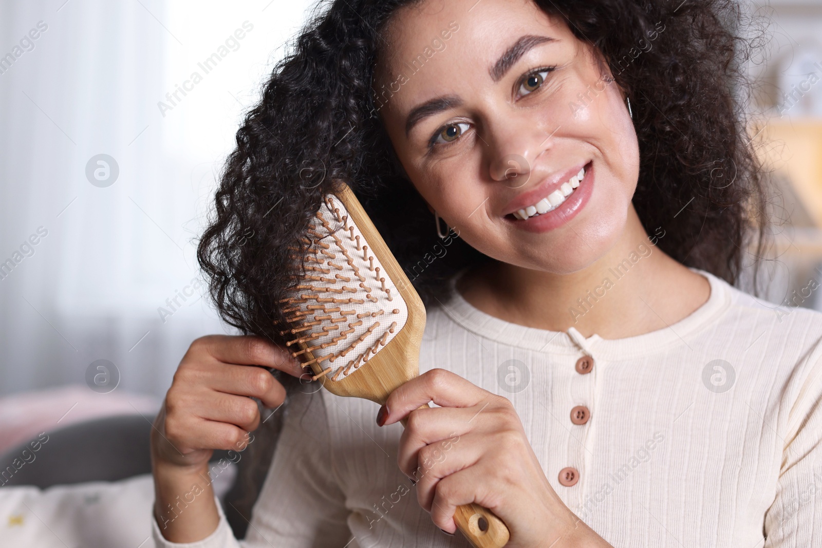 Photo of Smiling young woman brushing her curly hair at home