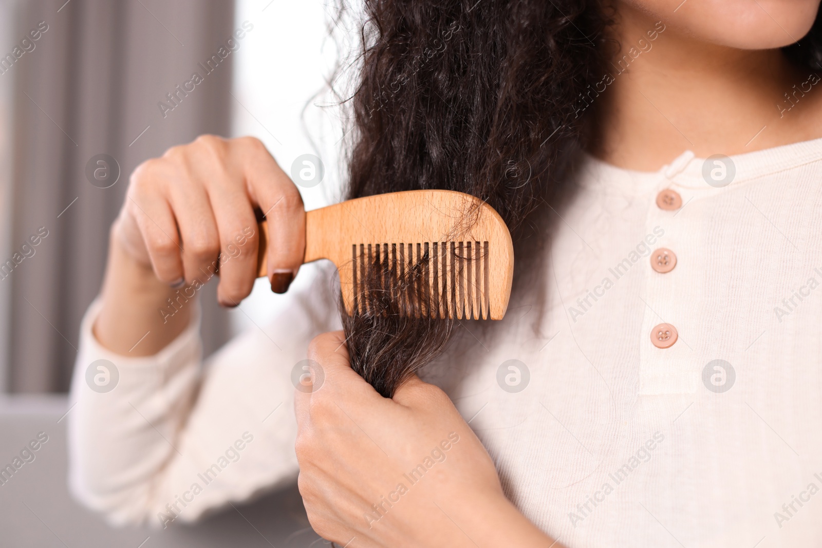 Photo of Woman brushing her curly hair with comb indoors, closeup