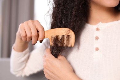 Photo of Woman brushing her curly hair with comb indoors, closeup