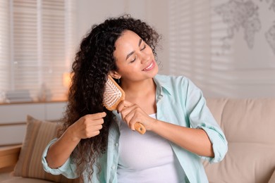 Smiling young woman brushing her curly hair at home