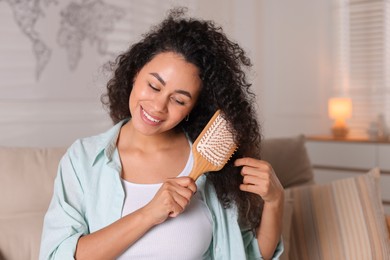 Photo of Smiling young woman brushing her curly hair at home