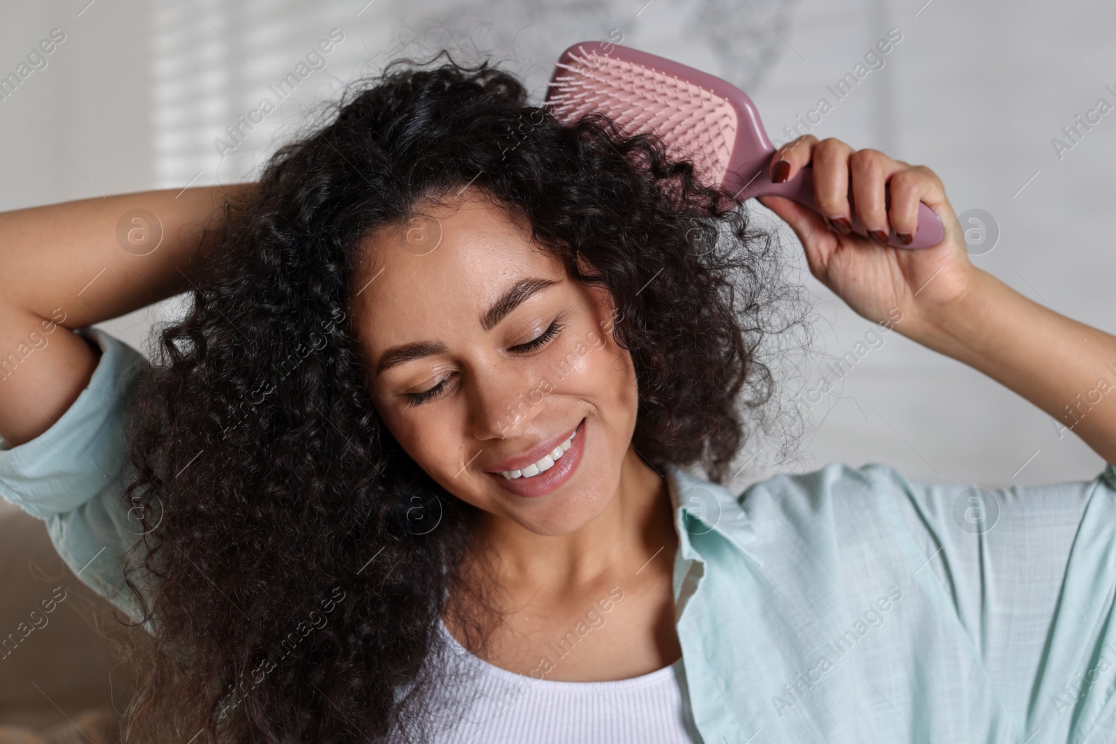 Photo of Smiling young woman brushing her curly hair at home