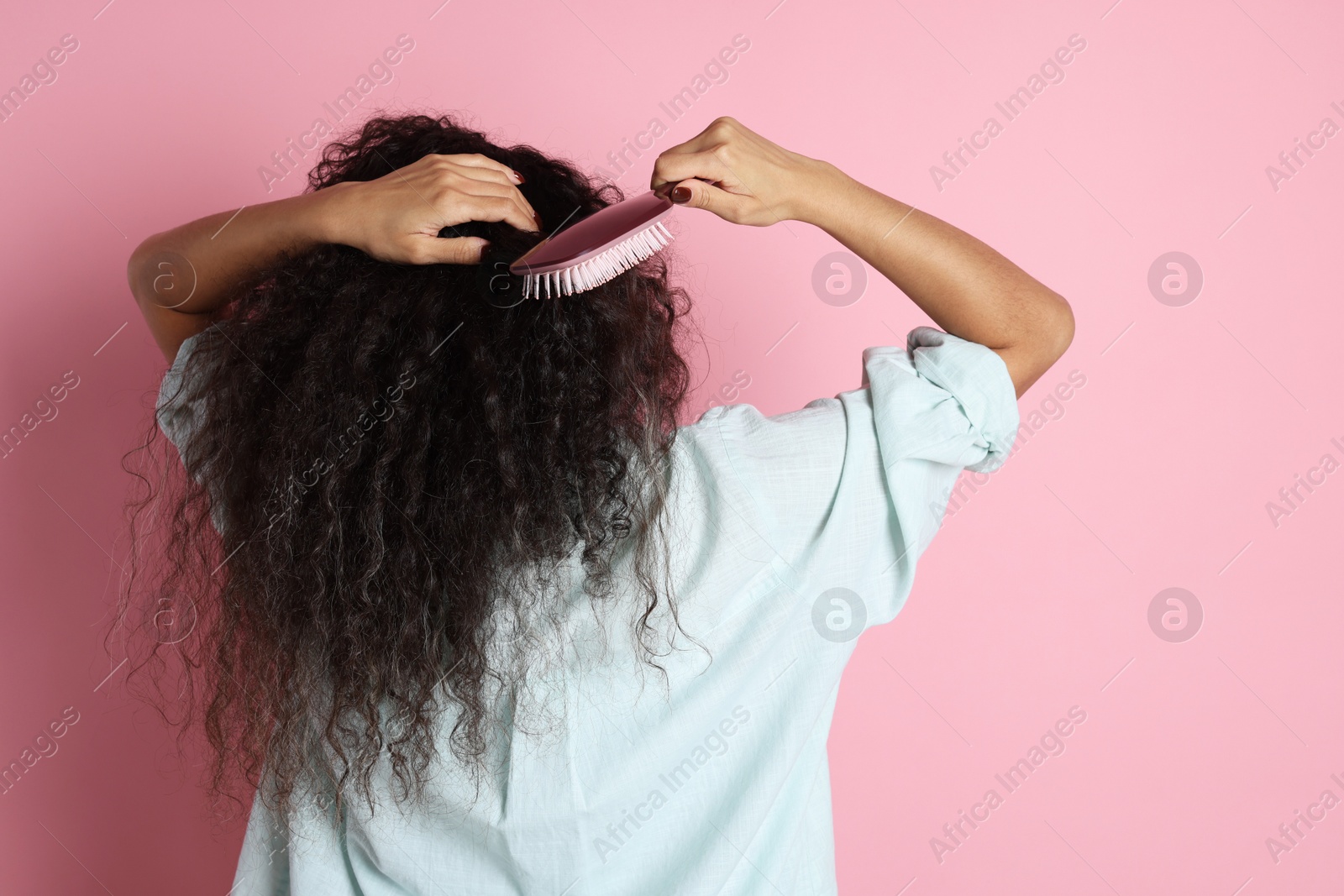 Photo of Woman brushing her curly hair on pink background, back view