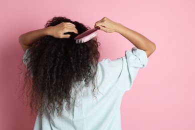 Photo of Woman brushing her curly hair on pink background, back view