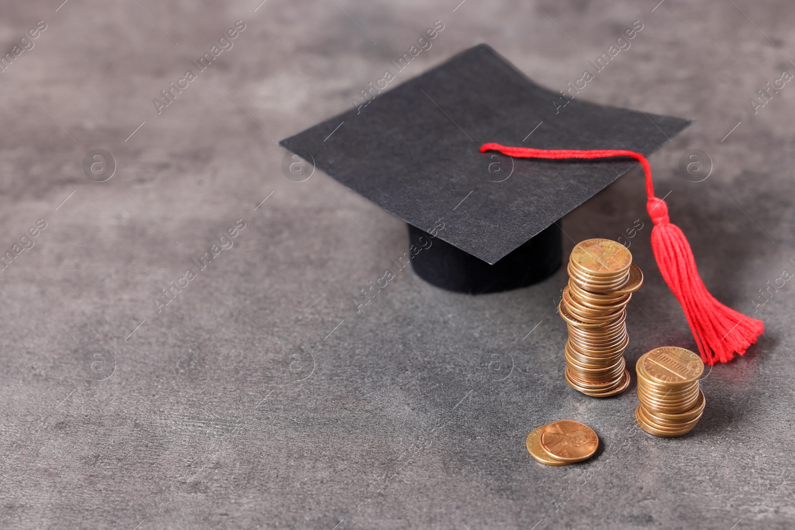 Photo of Graduate hat and coins on grey textured table, space for text. Tuition payment